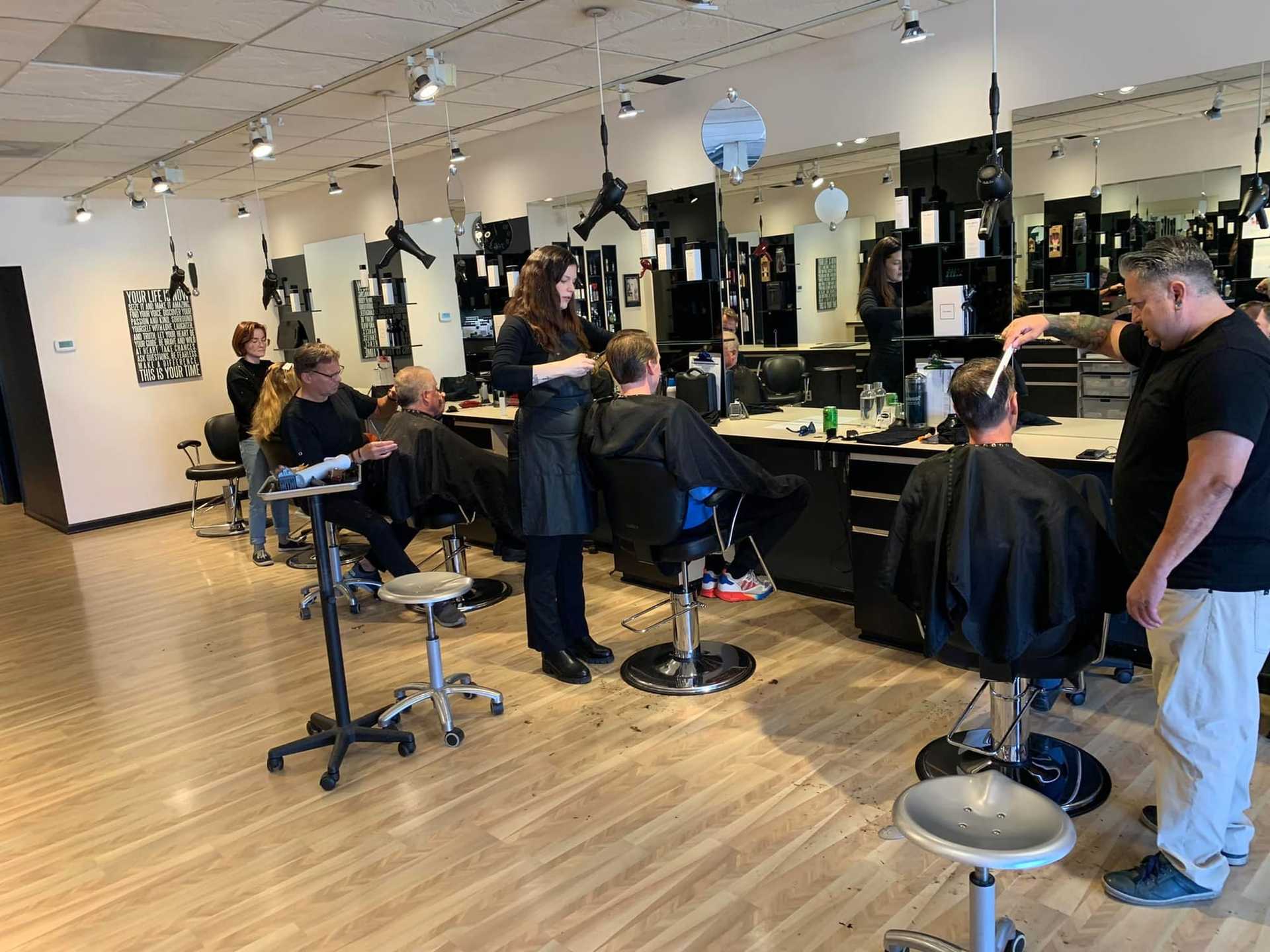 Customers receiving haircuts from stylists in a busy, modern salon.